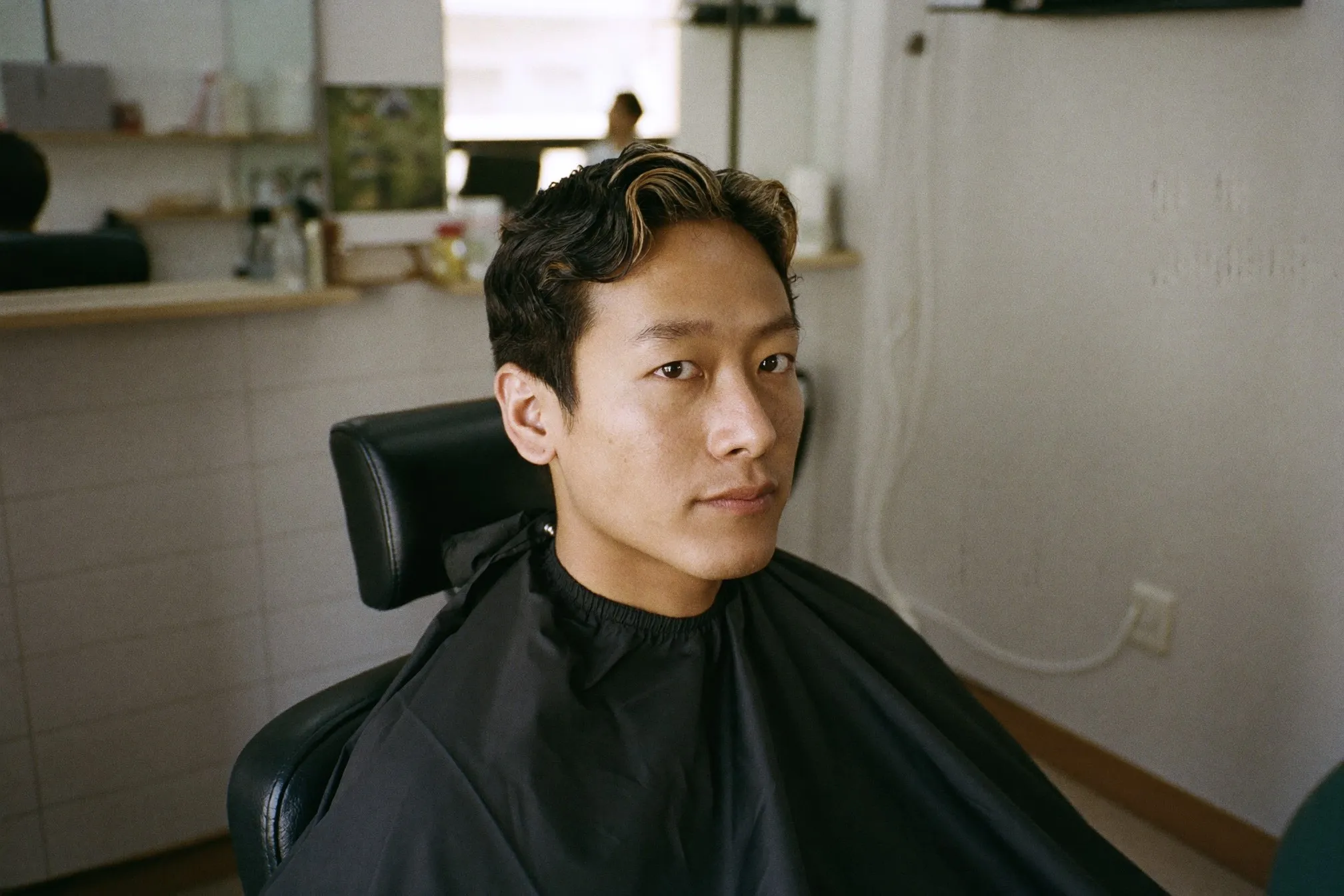Young Chinese Malaysian man with a soft permed wave on top sitting in a salon chair in Kuala Lumpur