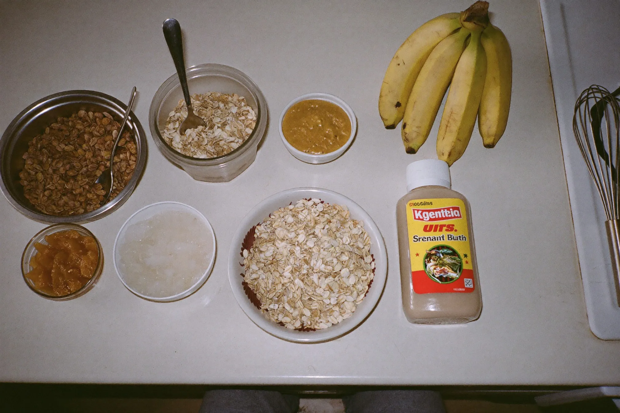 Overhead view of protein shake ingredients on an HDB kitchen counter: bananas, rolled oats, ice, peanut butter and a plain shaker bottle