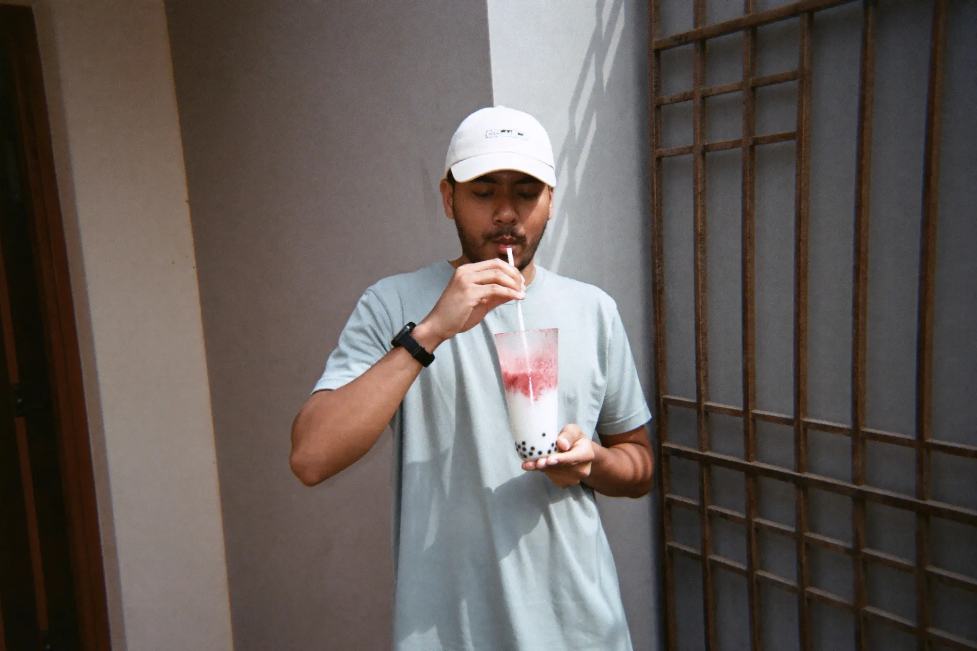 Indian Malaysian man drinking an iced protein shake from a tall glass at an outdoor fitness corner after training