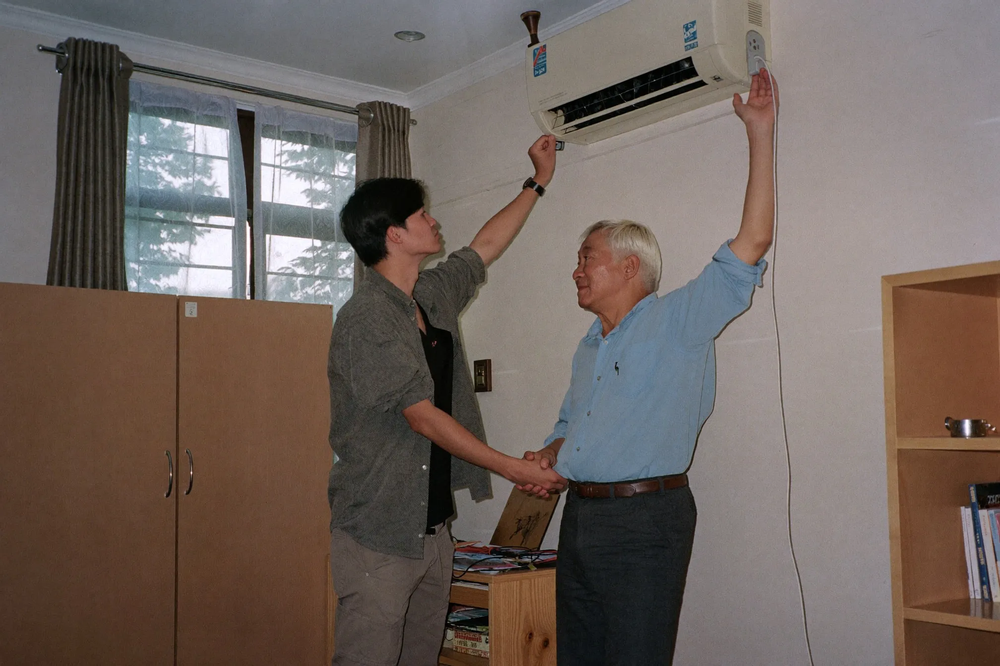 Two men inspecting the aircon unit and window in an HDB common room during a rental viewing