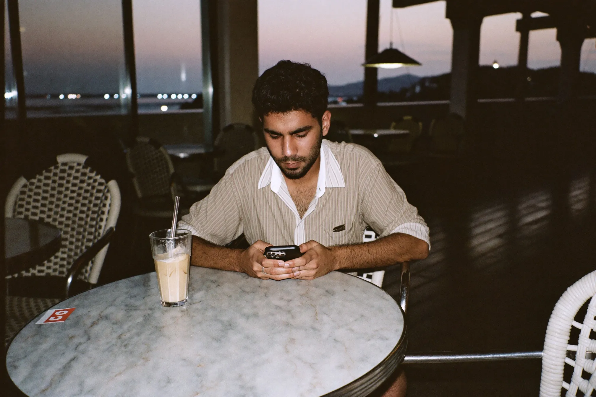 Man comparing room listings on his phone at a kopitiam table in the evening