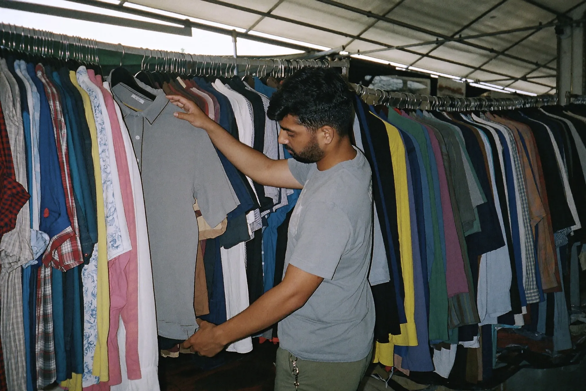 Man flicking through a rack of second-hand shirts at a weekend flea market stall