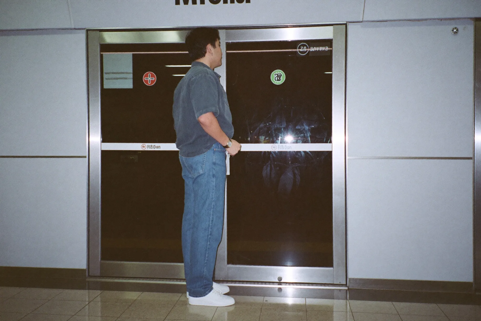 Man in a boxy 1990s-cut short-sleeve shirt and straight-leg jeans waiting on an MRT platform in Singapore