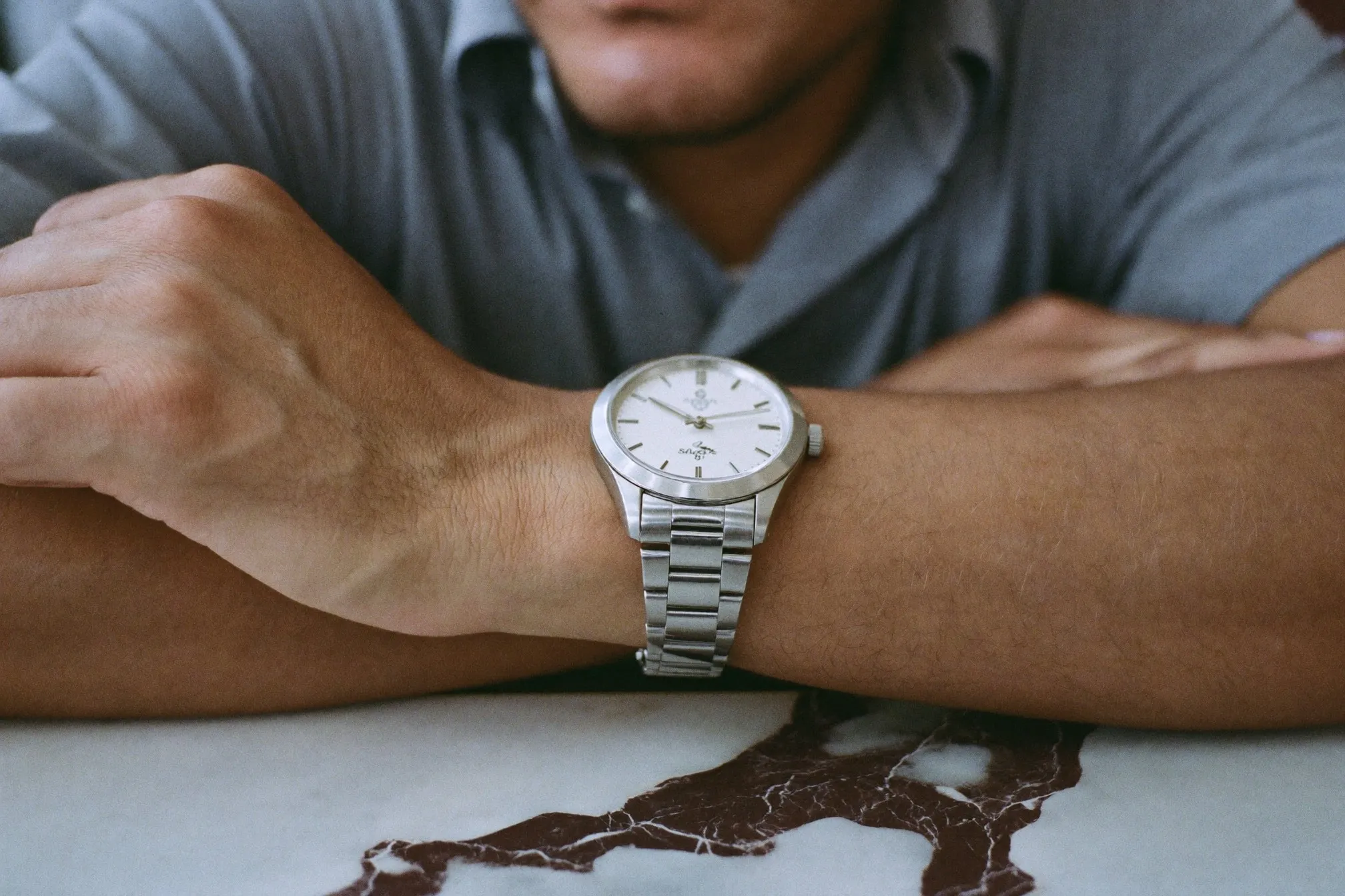 Close view of a plain unbranded steel sports watch on a man's wrist resting on a marble bar counter in Singapore
