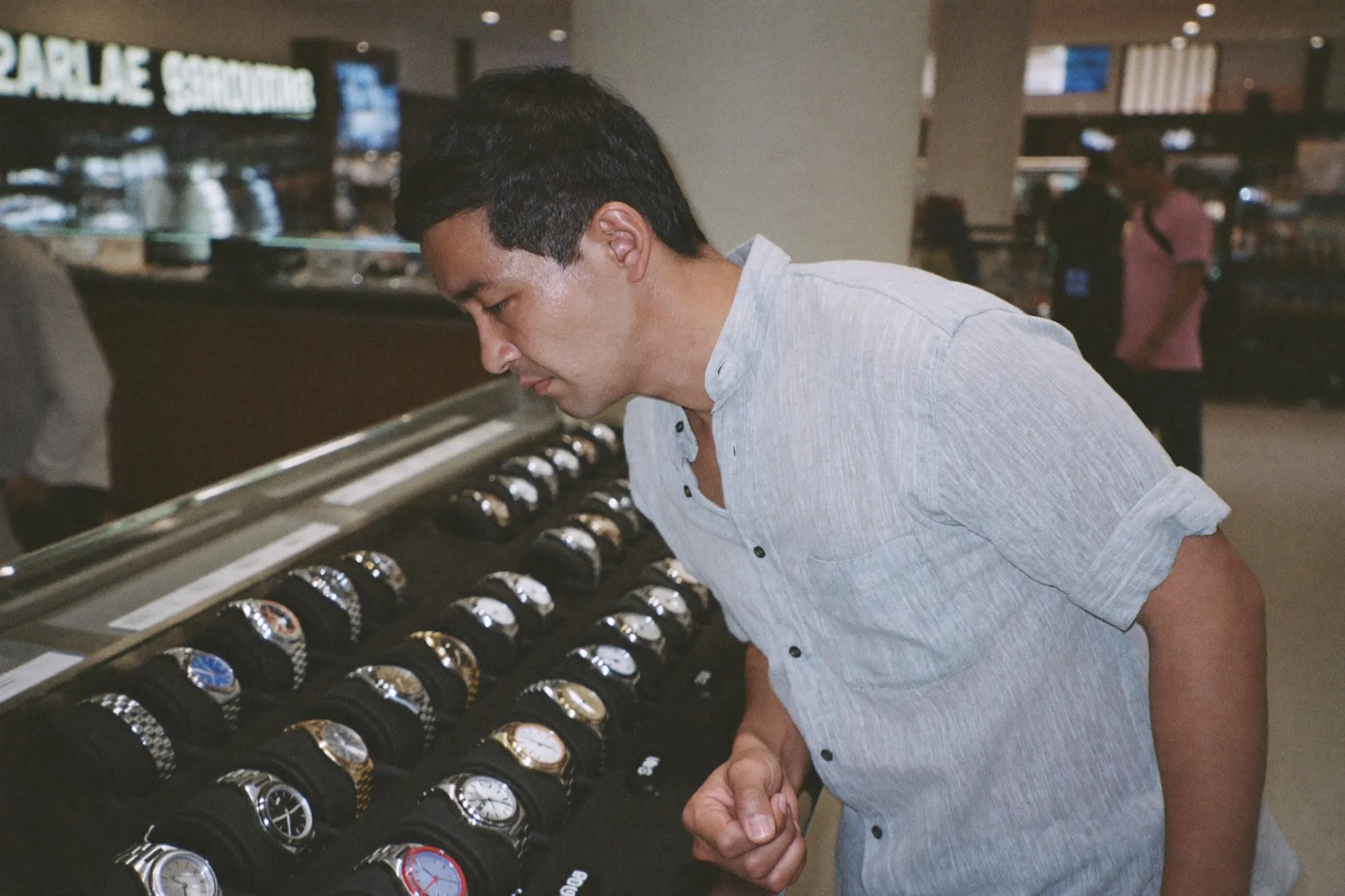 Man in a linen shirt looking at a plain unbranded steel sports watch on a tray at a mall watch counter in Kuala Lumpur