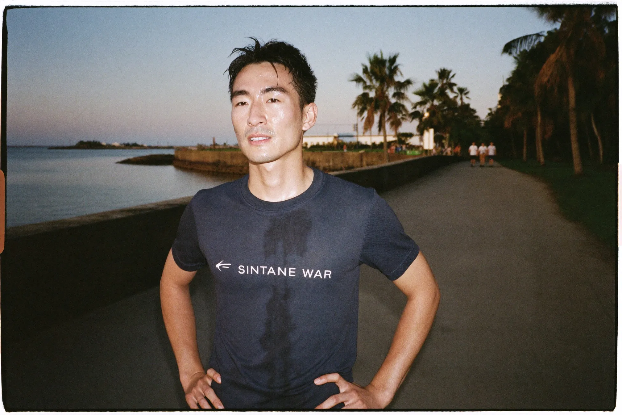 Chinese Singaporean man taking a walk break on a waterfront park connector at dusk, shirt soaked through