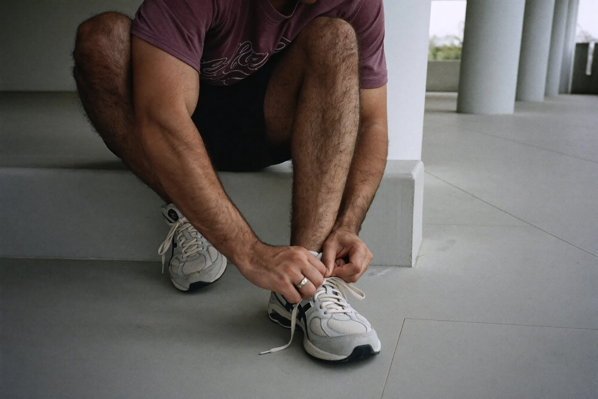 Indian man tying the laces of plain running shoes on a step at an HDB void deck early in the morning