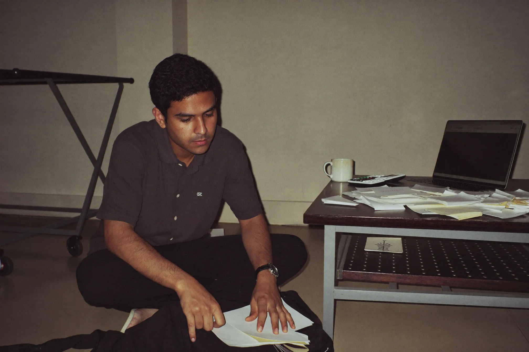 Man sitting on the floor of a small flat sorting through receipts and bank statements with a laptop open