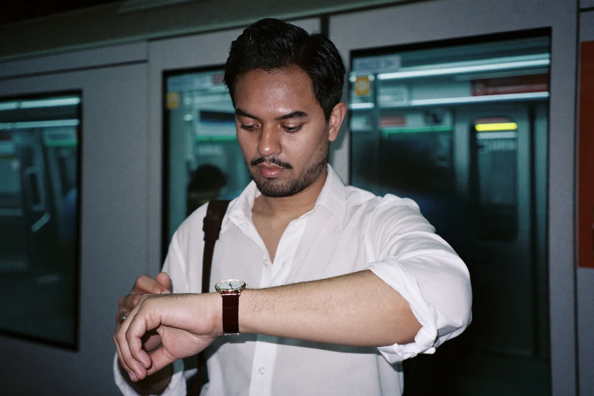 Man in a white shirt checking a slim automatic watch on a leather strap while waiting on an MRT platform in Singapore