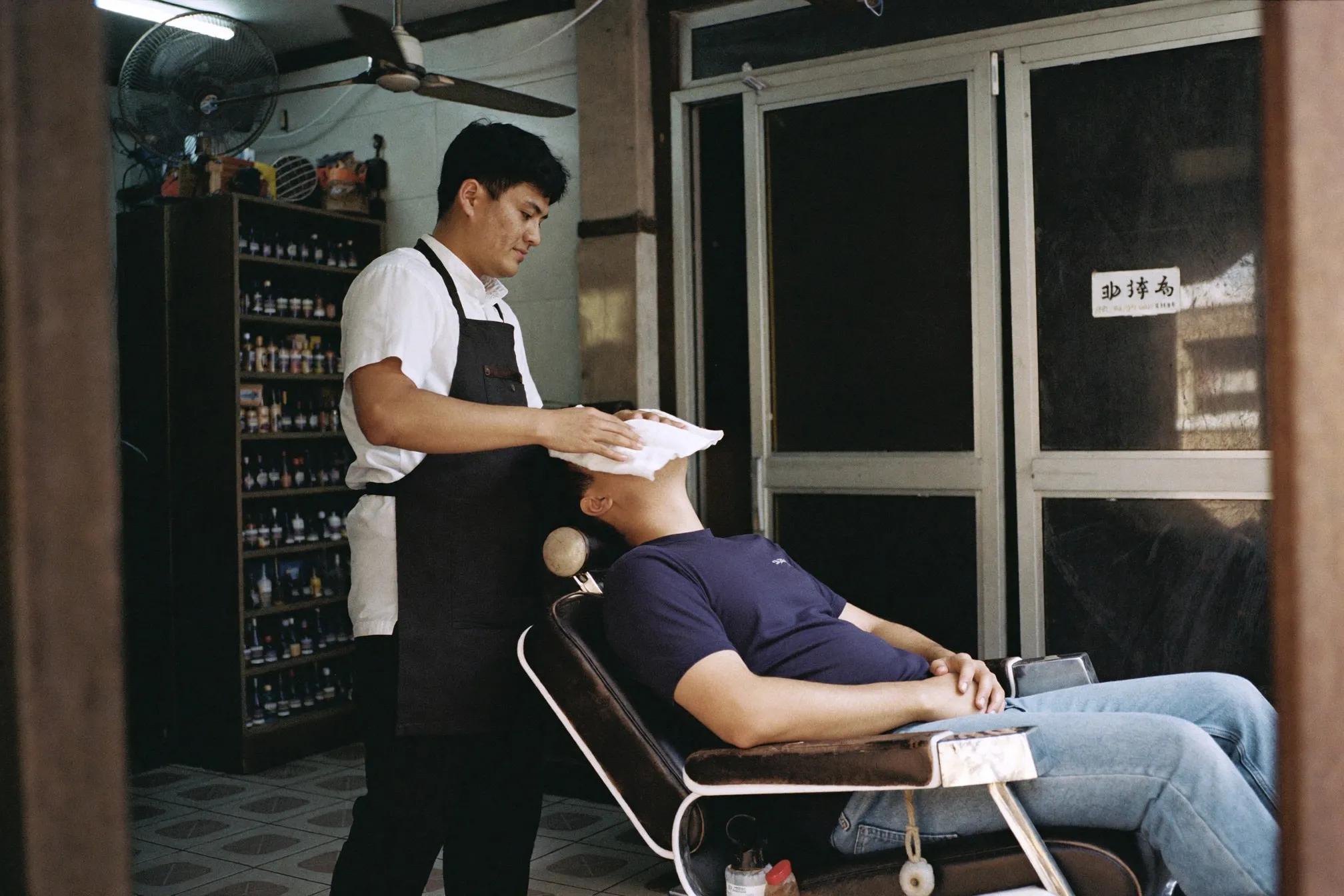 Barber laying a hot towel over a seated client's face in a neighbourhood barbershop