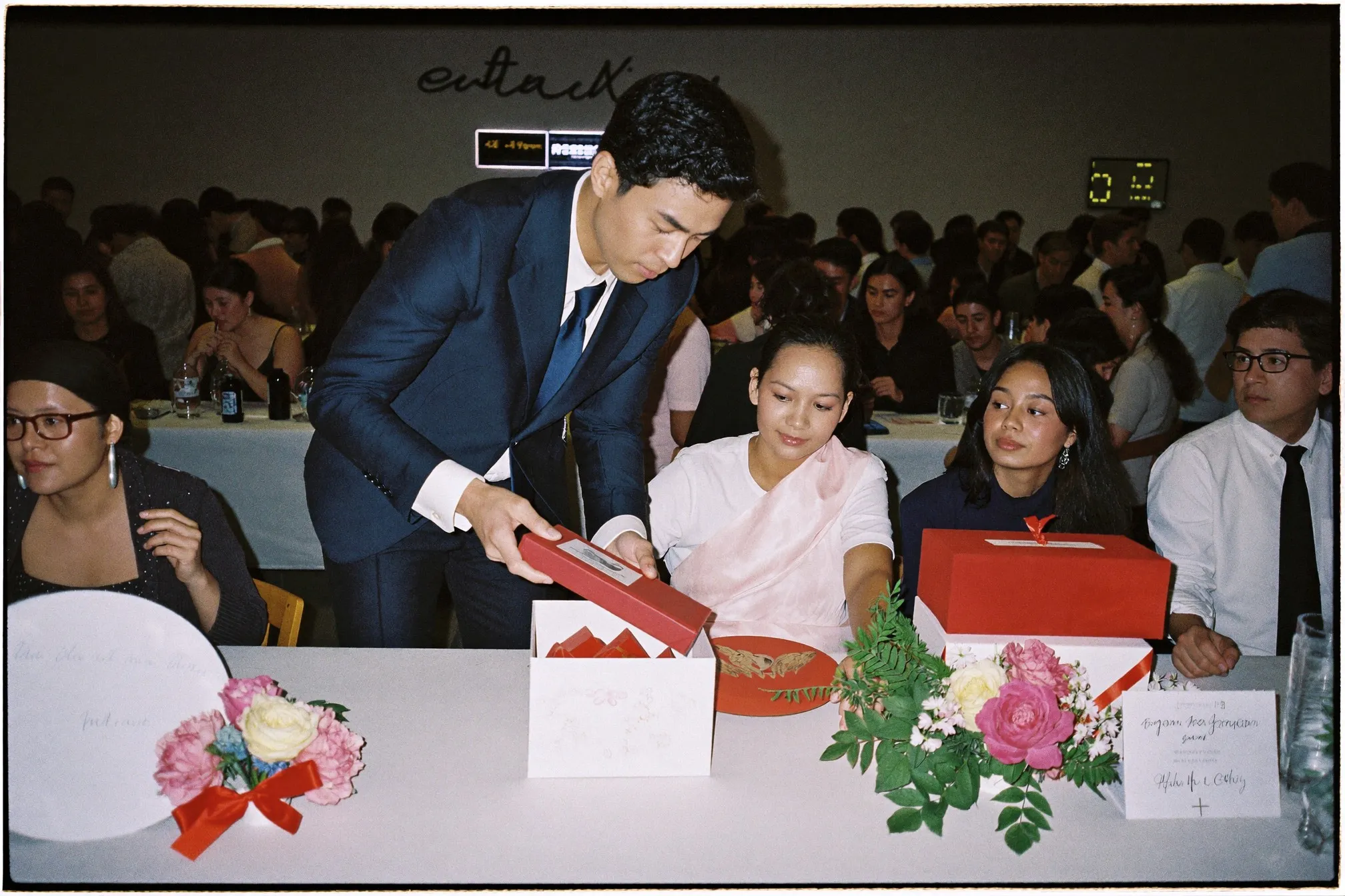 Man in a navy blazer placing a red packet into a decorated box at a wedding sign-in table