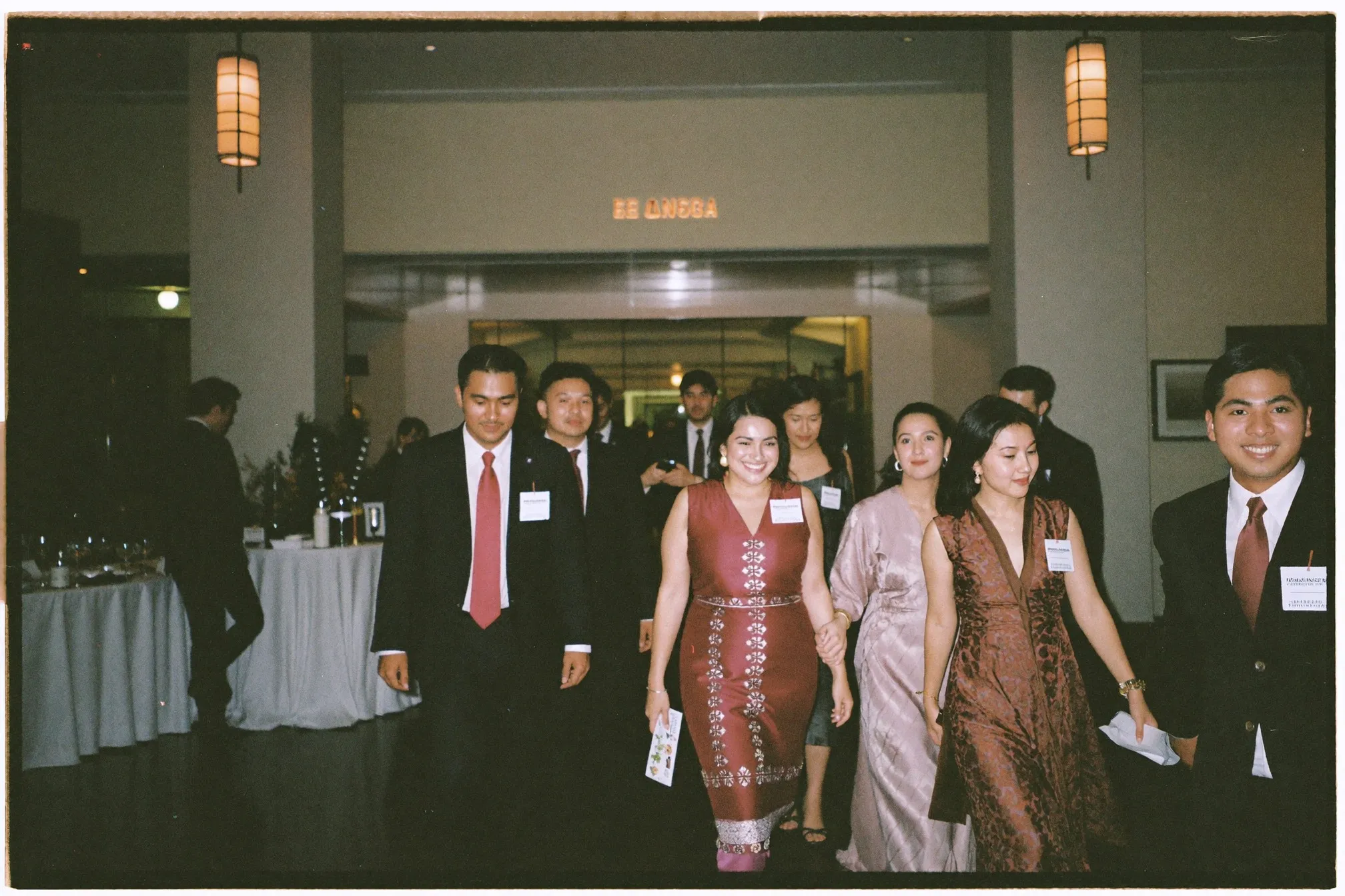 Wedding guests in smart attire arriving at a hotel ballroom foyer with a reception table