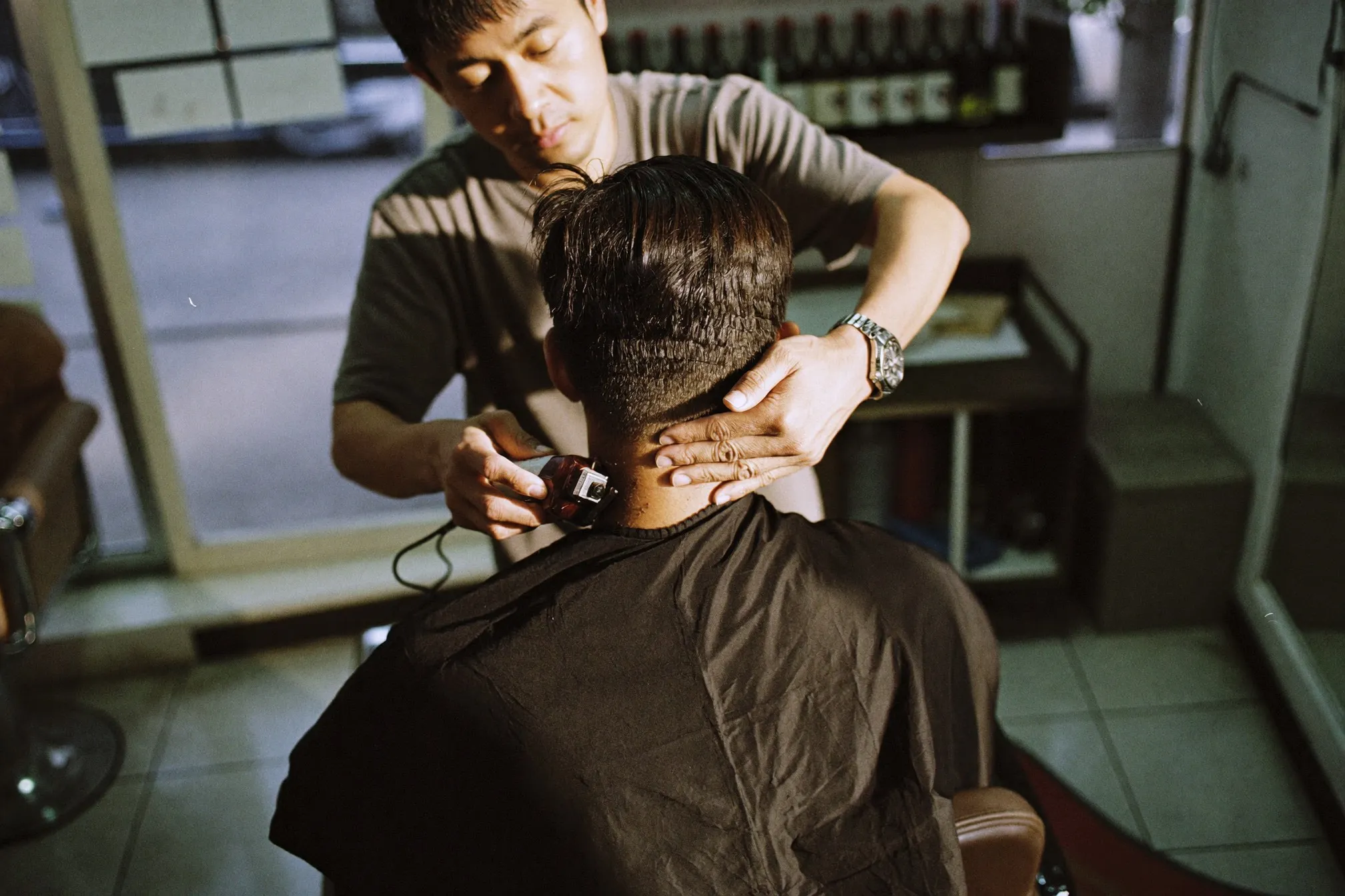 Barber cleaning up the back of a client's neck with clippers in a neighbourhood barbershop