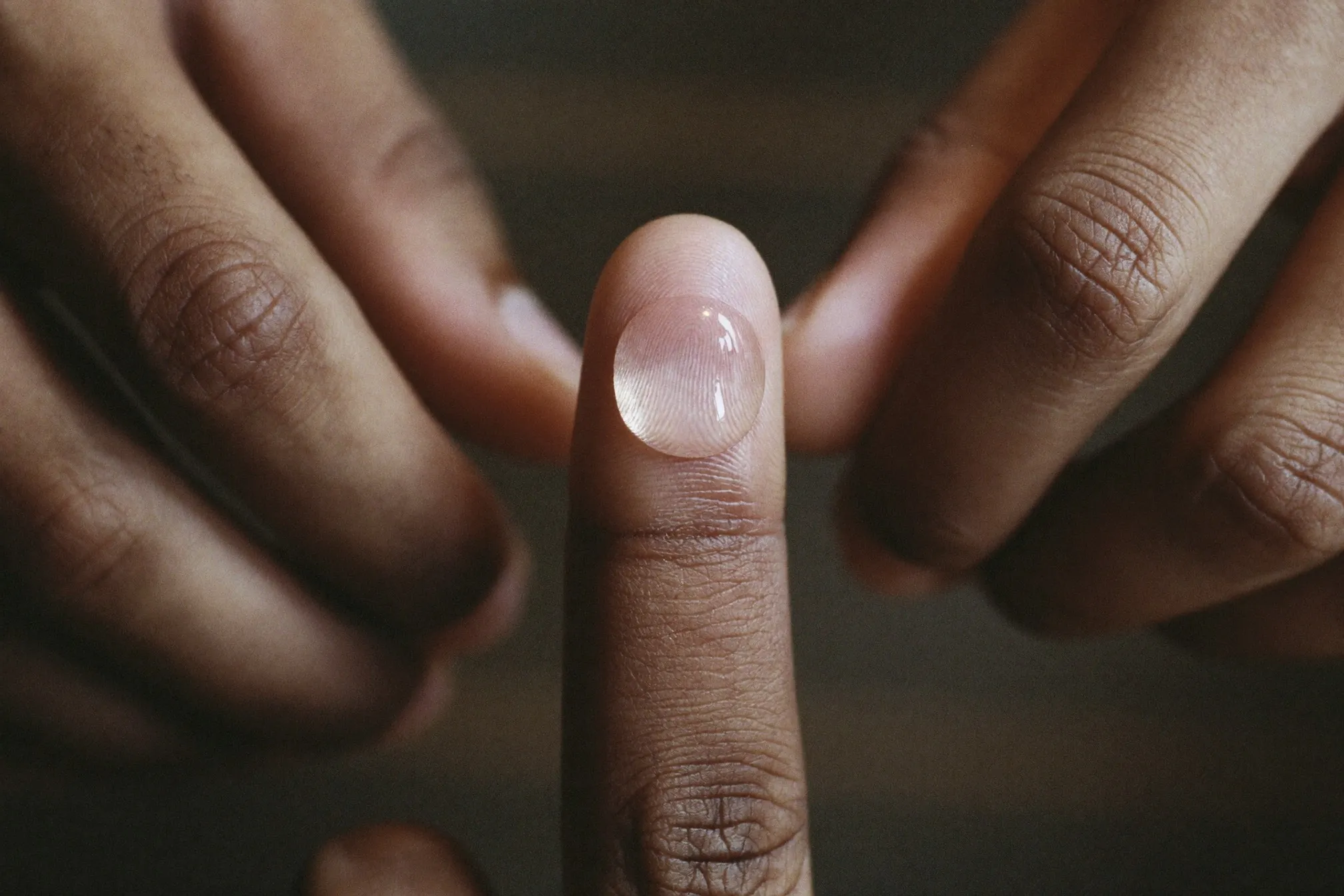 Close view of a single drop of clear serum on a man's fingertip under warm bathroom light