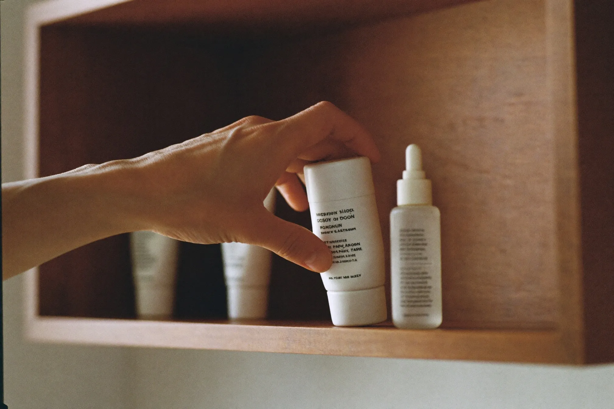 Man's hand reaching for one of three unbranded skincare bottles on a bathroom shelf