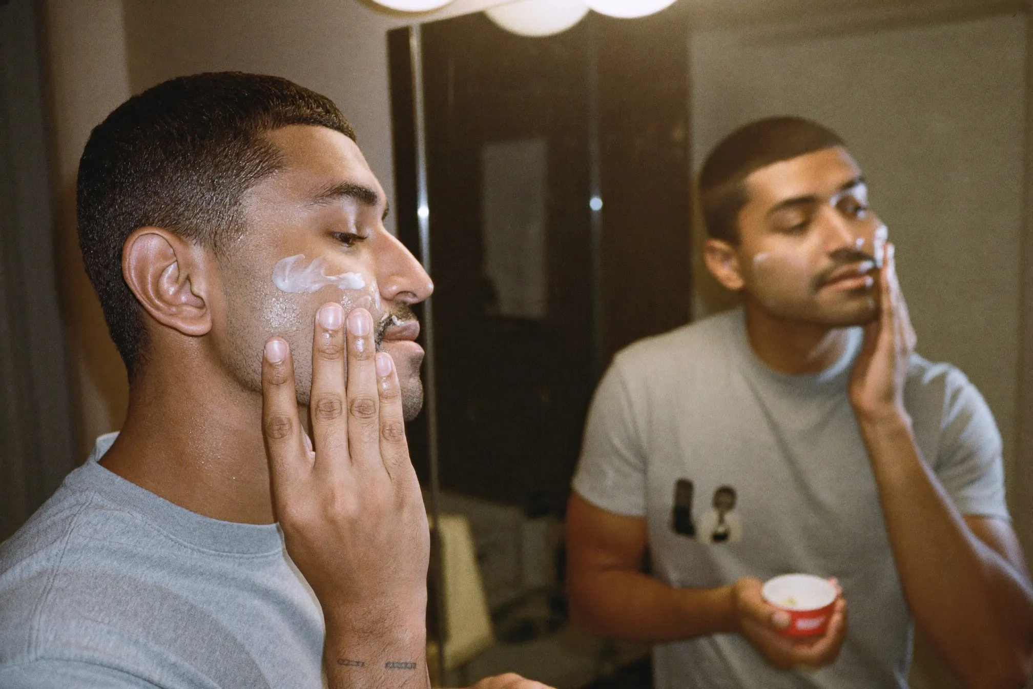 Man applying moisturiser to his face in front of a bathroom mirror after shaving