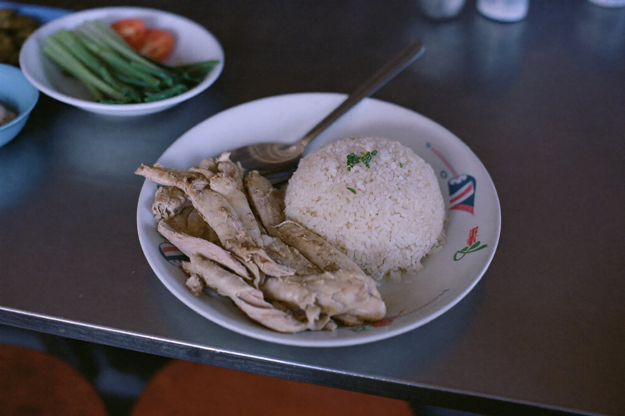 Plate of steamed chicken rice with an extra portion of chicken and a side of green vegetables at a Singapore hawker centre