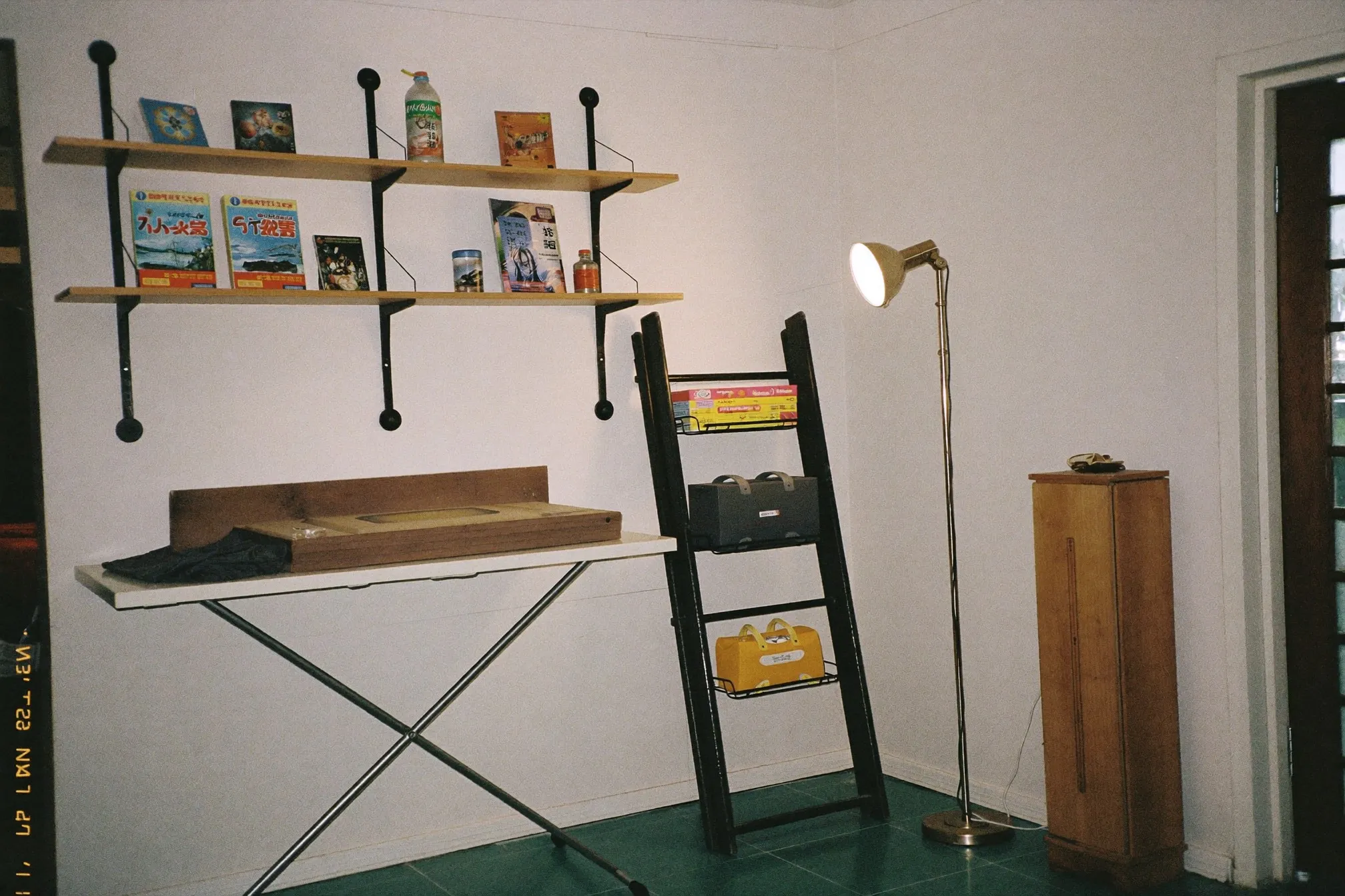 Corner of a small HDB flat with a folding dining table, wall shelves and a floor lamp