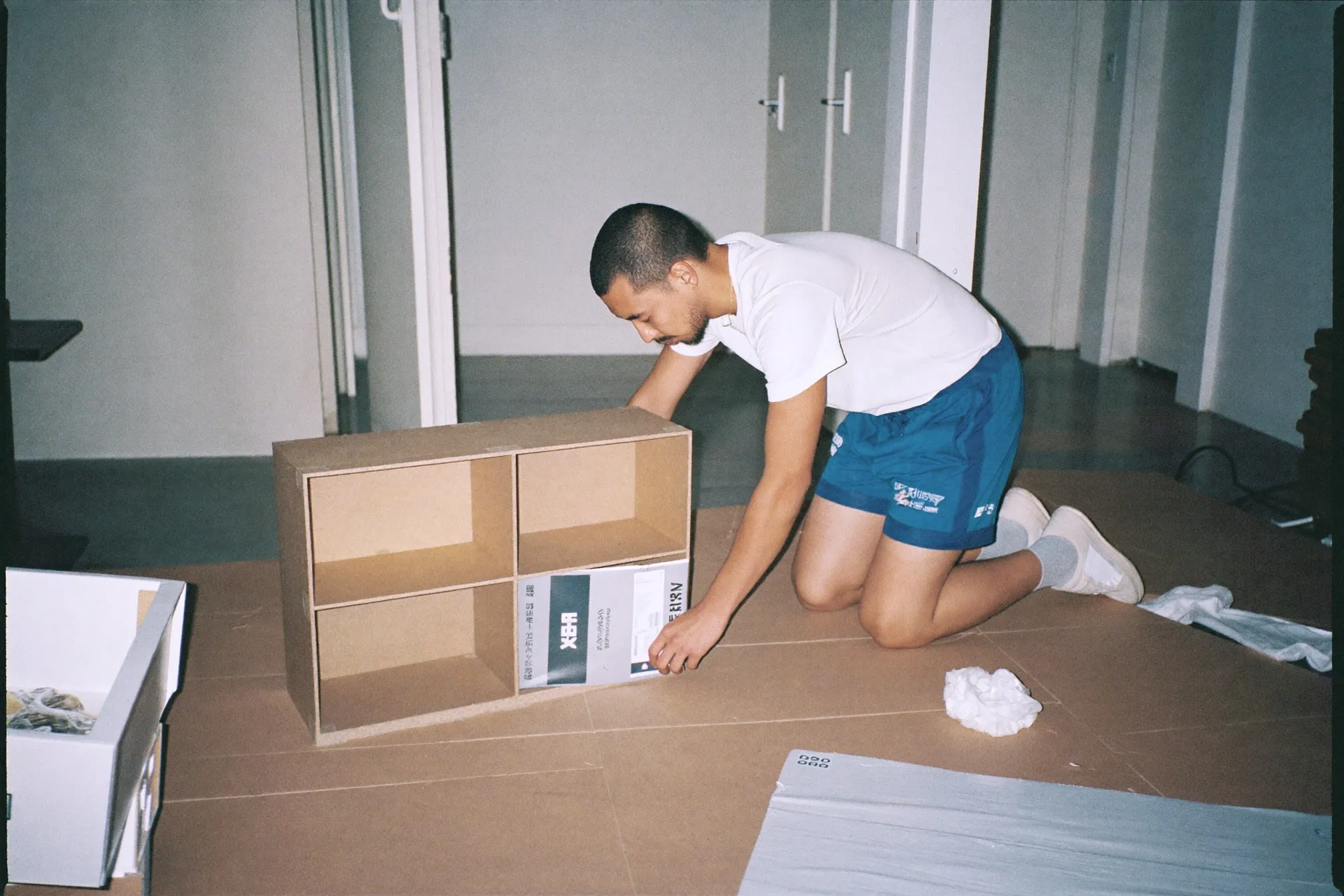 Man assembling a flat-pack shelf unit on the floor of a bare studio apartment in Singapore