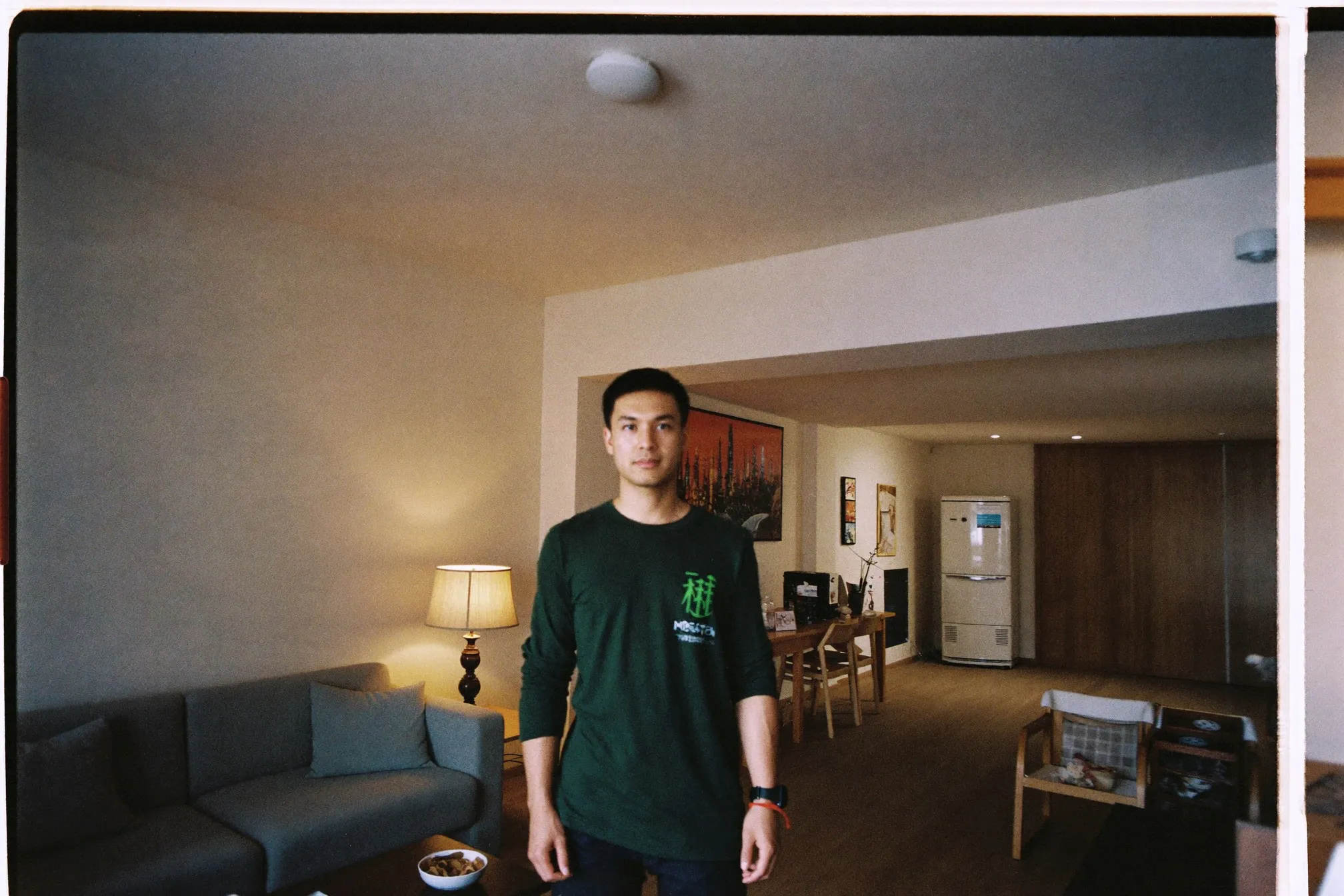 Man standing in the living area of a small Kuala Lumpur condo unit, warm lamp light, low sofa and open floor space