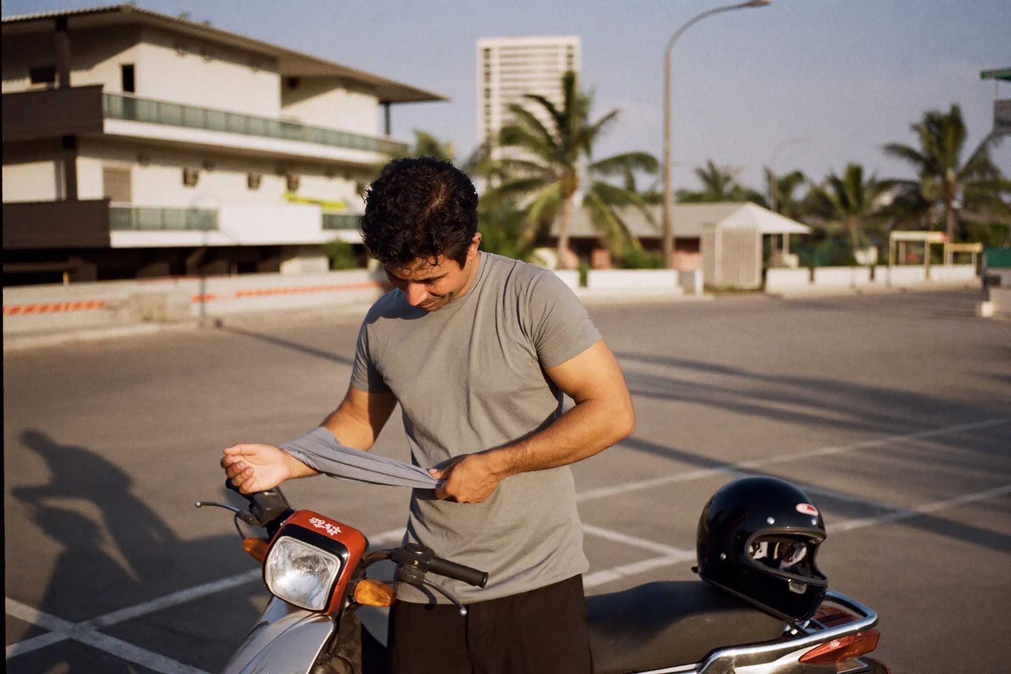 Rider pulling a plain grey UV sleeve over his forearm beside a motorbike in a Kuala Lumpur car park