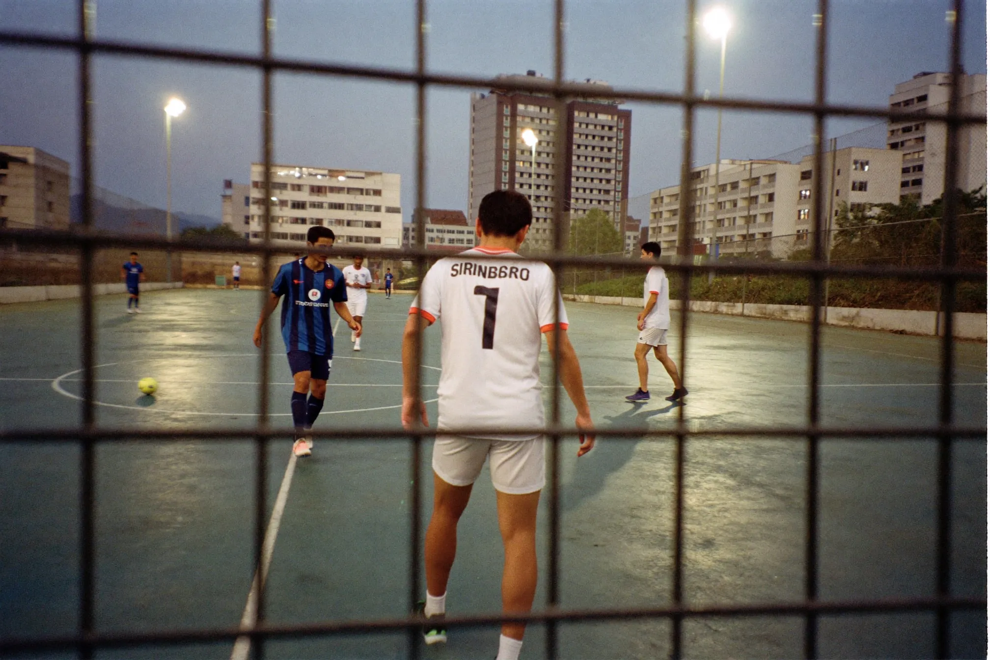 Men playing futsal under floodlights on an outdoor court at dusk in Singapore