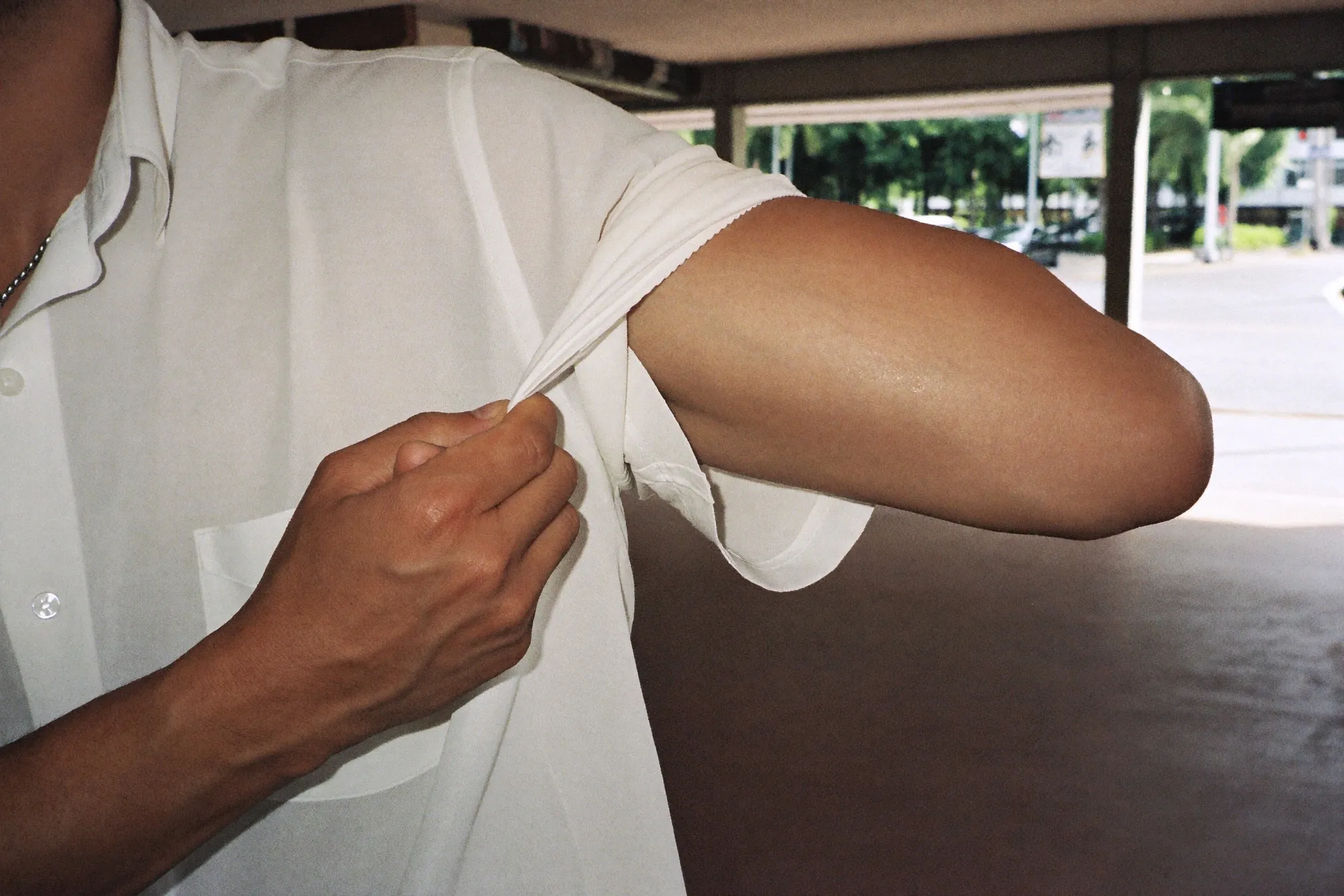 Man pushing up his shirt sleeve on a covered walkway, showing a clear tan line across his forearm