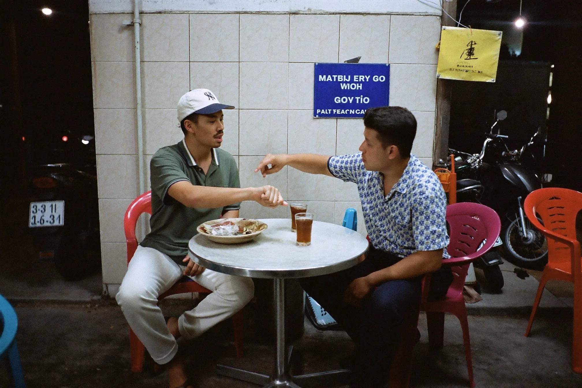 Two men talking over drinks at a late-night mamak table after a film