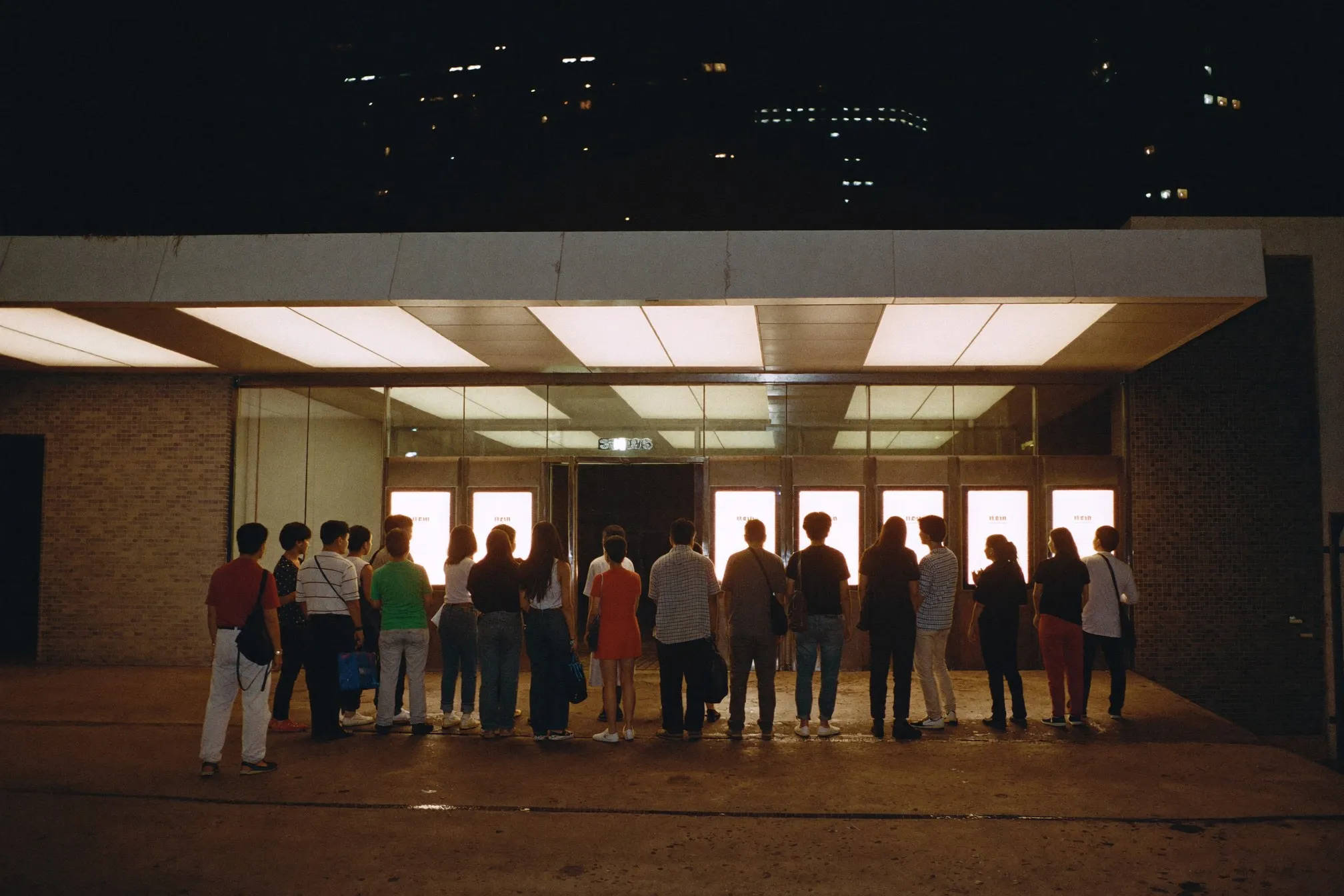 Illuminated cinema entrance at night in Kuala Lumpur with a queue of people waiting under the canopy