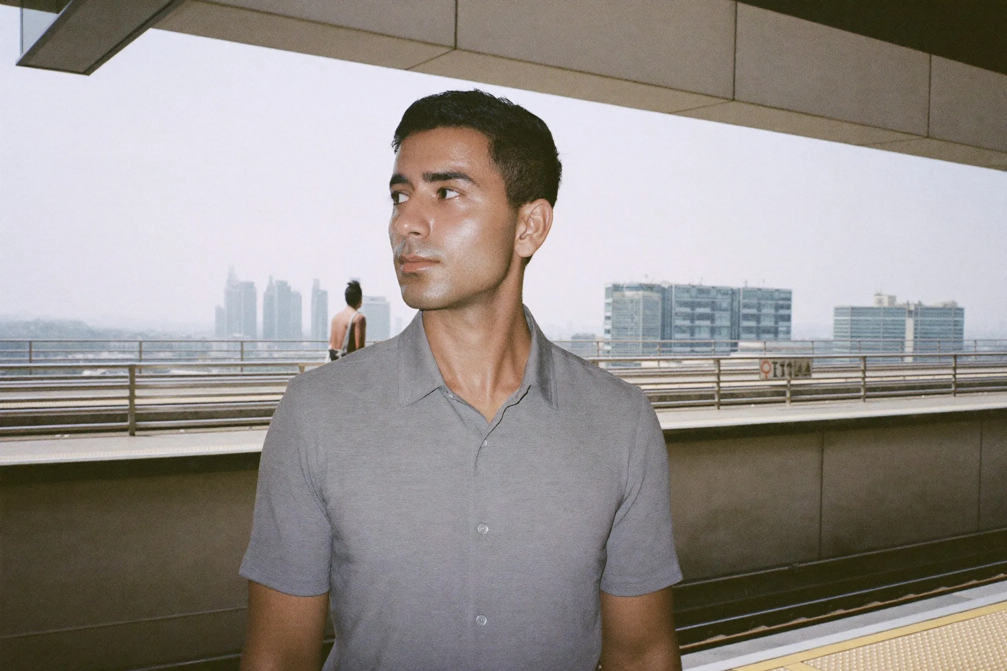 Man with an even matte complexion waiting on an open-air LRT platform at midday