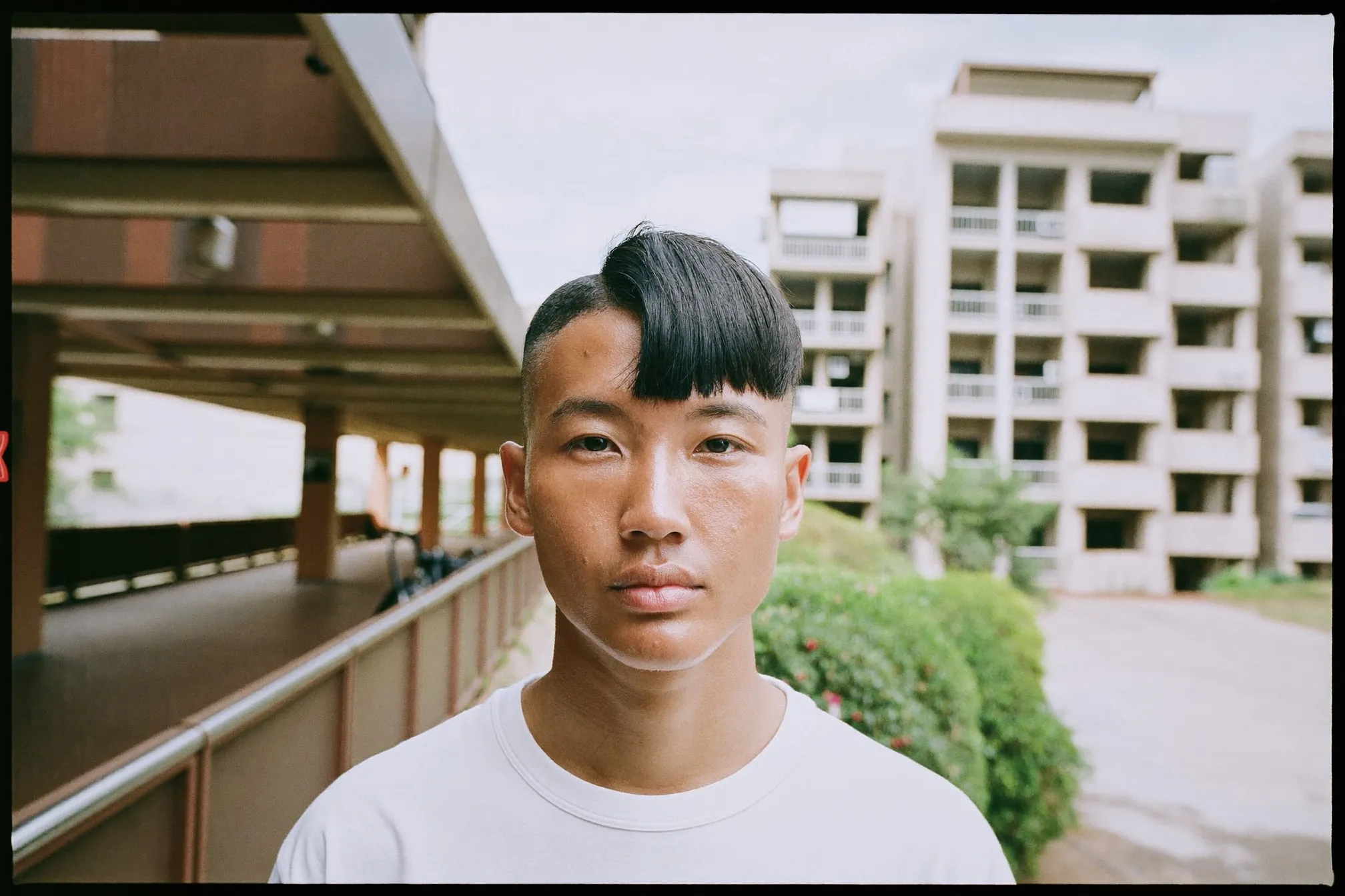 Young Malay man with a styled two block haircut standing along a covered walkway outside HDB flats in Singapore