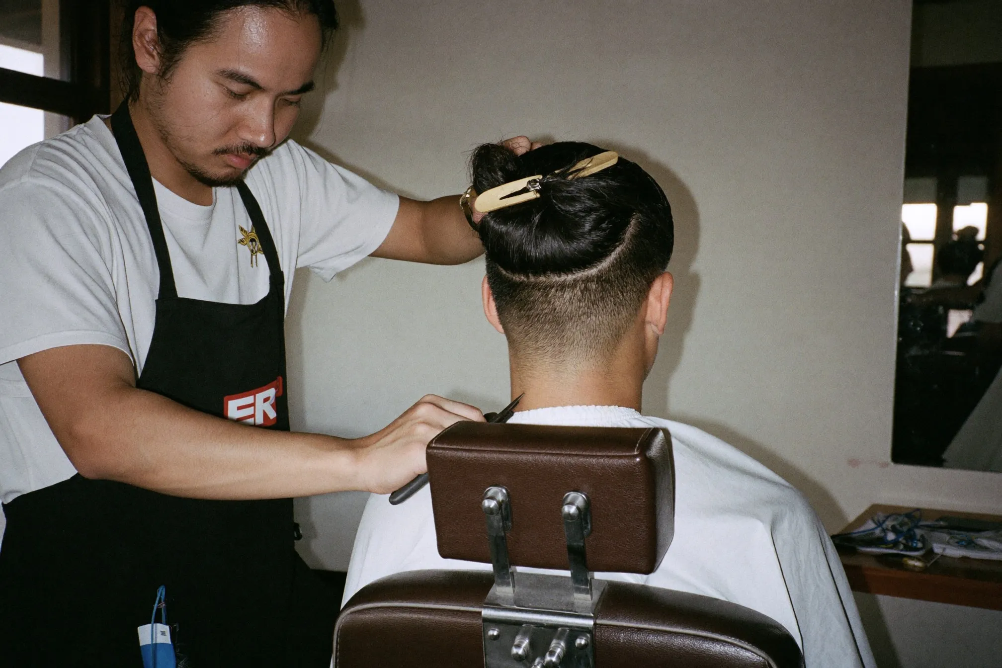 Barber clipping the short back and sides of a two block haircut on a young Chinese Malaysian man in a KL barbershop