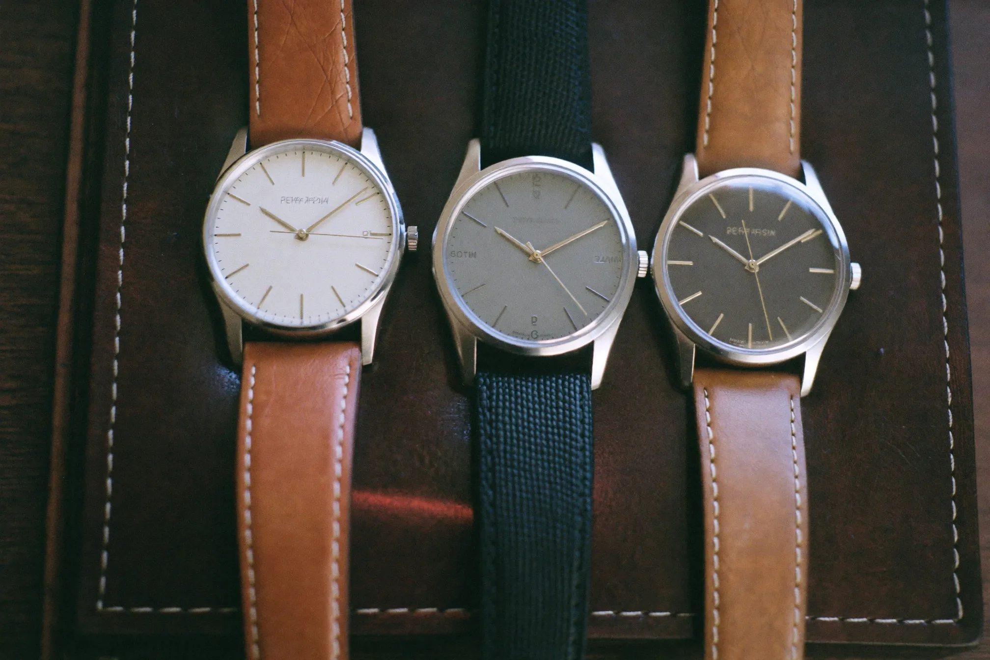 Three generic unbranded watches with different dial colours laid on a leather tray