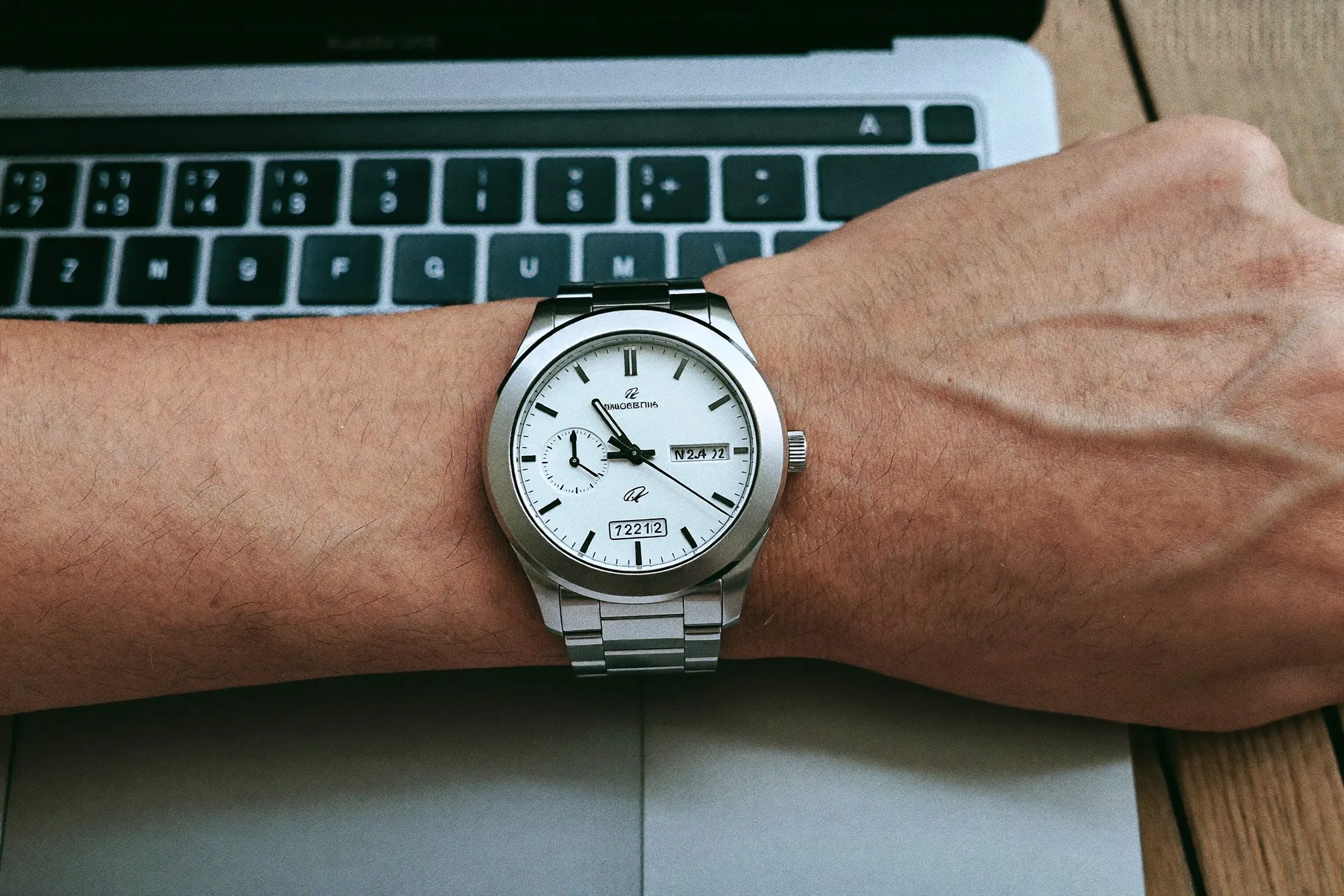 Close view of an unbranded automatic watch on a man's wrist beside a laptop keyboard