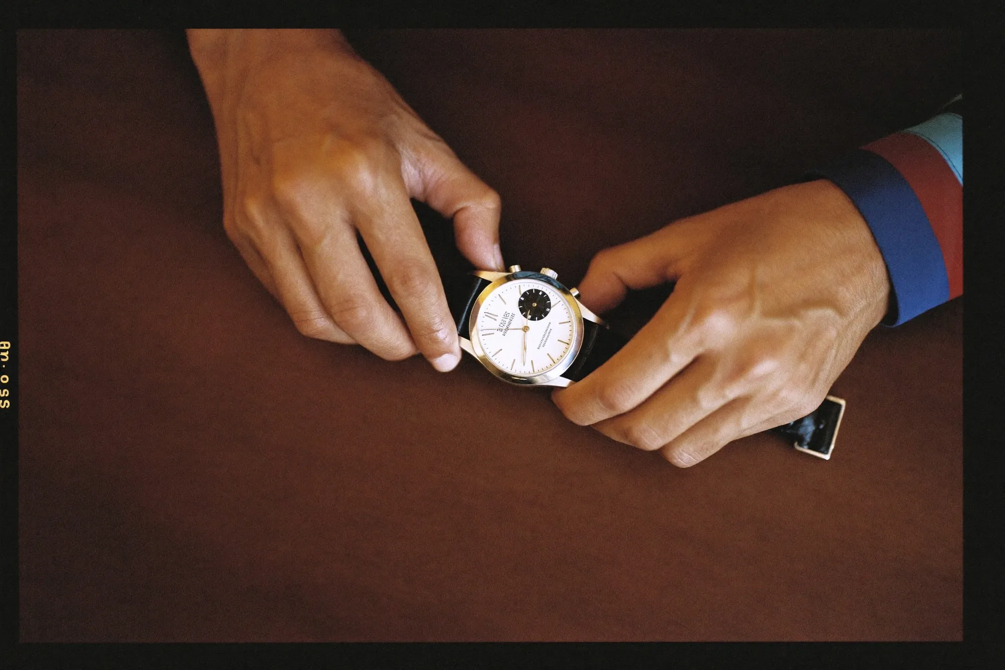 Man examining a plain unbranded automatic watch under a warm lamp at a wooden desk