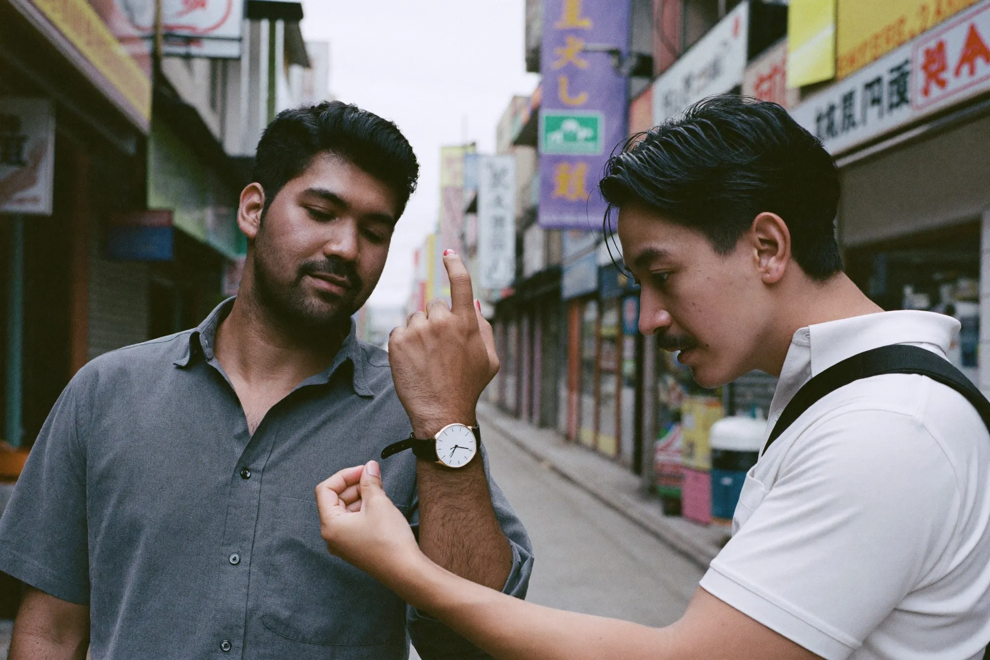 Two friends comparing the watches on their wrists outside a shophouse in Singapore