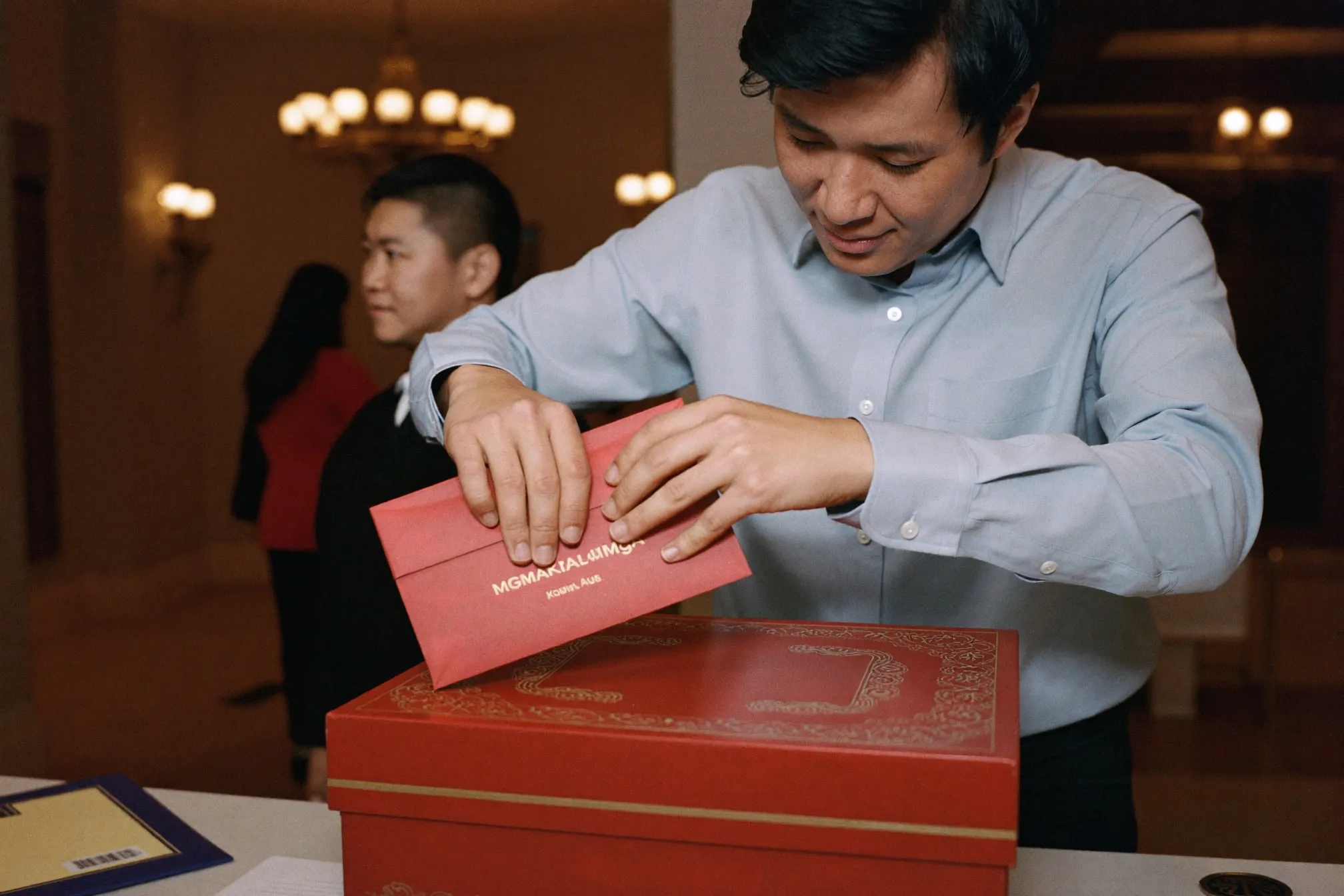 Wedding guest placing a red packet into a gift box at a hotel ballroom reception desk in Kuala Lumpur