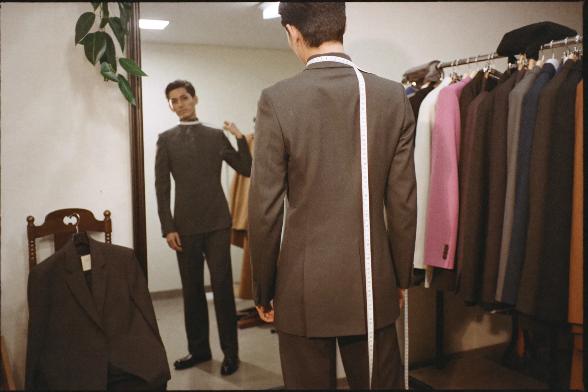 Man checking the shoulder fit of a charcoal blazer in a tailor shop mirror before a wedding