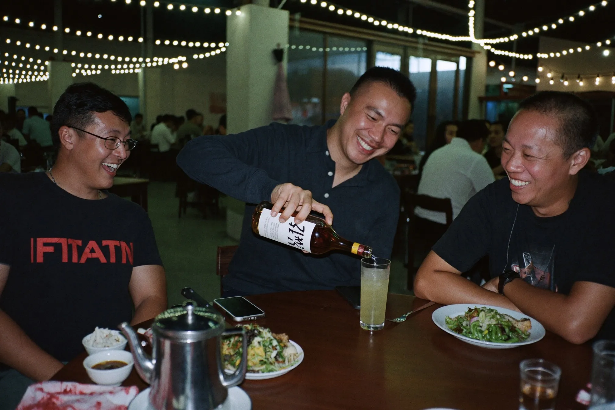 Two friends pouring whisky over ice at a round table at an open-air Chinese restaurant in Kuala Lumpur