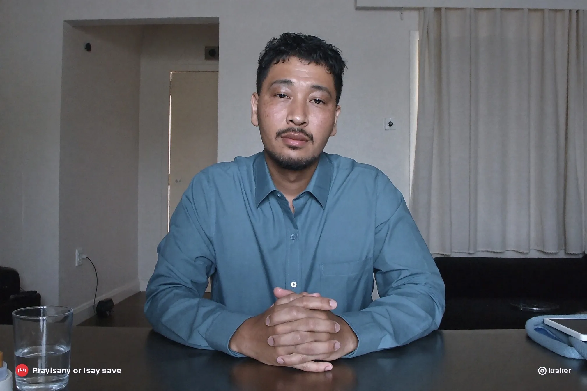 Man on a video call at a small dining table in an HDB flat, wearing a mid-blue collared shirt